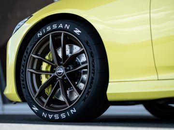 Close-up van het voorwiel van een gele Nissan Z Proto, met de Dunlop-banden en gedetailleerde remcomponenten.