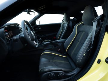 Binnenaanzicht van een Nissan Z Proto met zwarte en gele stoelen, stuurwiel en dashboard zichtbaar, deur open.