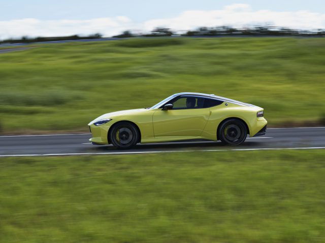Gele Nissan Z Proto rijdt te hard op een snelweg met een wazig groen landschap op de achtergrond.
