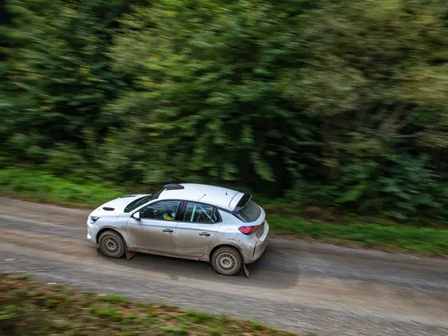 Een Opel Corsa Rally4 snelt over een bochtige bosweg, vastgelegd met bewegingsonscherpte die de snelheid benadrukt.