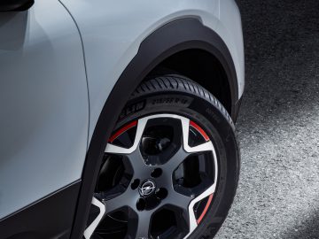 Close-up van het achterwiel van een Opel Mokka met gedetailleerd zicht op het loopvlak en de stijlvolle velg, tegen een schaduwrijke achtergrond.