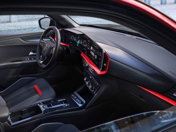 Binnenaanzicht van de Opel Mokka vanaf de passagierszijde met een stuur, een digitaal dashboard en een middenconsole met rode accenten.