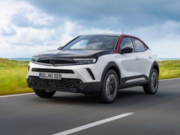 Een witte Opel Mokka SUV rijdt op een kustweg onder een helderblauwe lucht.