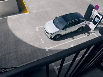 Een witte Peugeot 3008 elektrische auto geparkeerd en opgeladen bij een station op een parkeerplaats op het dak, van bovenaf gezien.