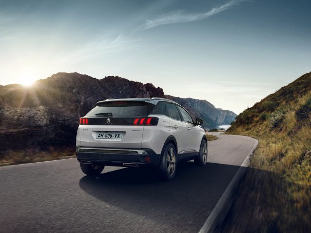 Een witte Peugeot 3008 elektrische SUV die bij zonsondergang op een bochtige weg door bergachtig terrein rijdt.