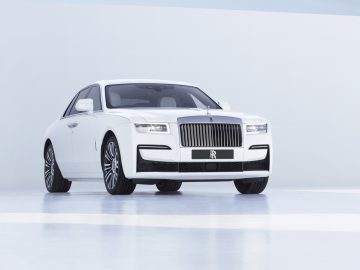 Een witte Rolls-Royce Ghost geparkeerd in een studio met een lichtblauwe achtergrond, waardoor het vooraanzicht en de grille goed zichtbaar zijn.