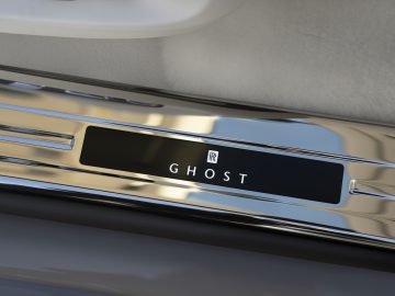 Close-up van de gepolijste chromen instaplijsten met het opschrift "Ghost" en het Rolls-Royce-logo op een luxe auto van Rolls-Royce Ghost.