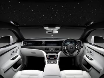Binnenaanzicht van een Rolls-Royce Ghost met witleren stoelen, een gedetailleerd dashboard en een hemelbekleding met sterrenlicht.