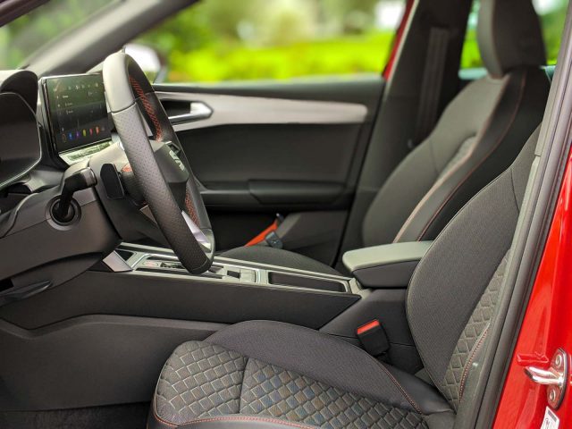 Interieur van een Seat Leon Sportstourer met een gedetailleerd overzicht van de bestuurdersstoel, het dashboard en het stuur, met de deur open.