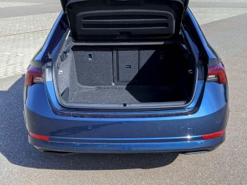Open kofferbak van een blauwe Skoda Octavia met een ruim, schoon interieur onder fel zonlicht.