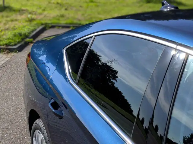 Blauwe Skoda Octavia, buiten geparkeerd, met details van de glanzende achterkant en het raam dat bomen en de lucht weerspiegelt.