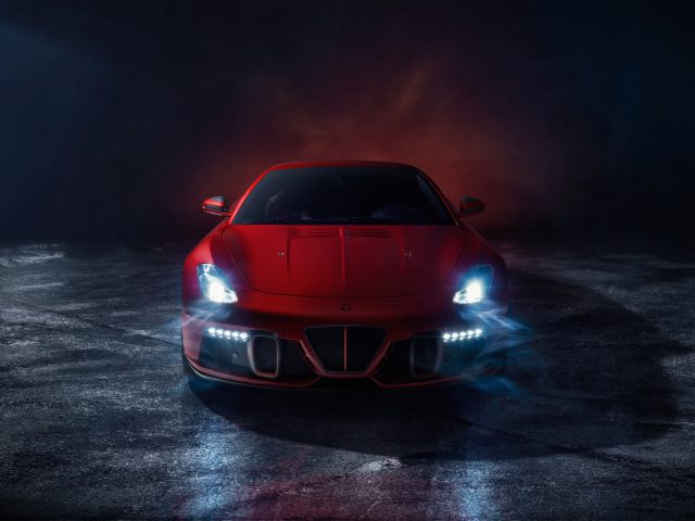 Rode AERO 3-sportwagen met verlichte koplampen geparkeerd in een donkere, mistige omgeving, waardoor een dramatische en mysterieuze sfeer ontstaat.