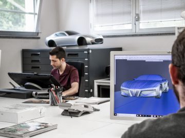 Twee mannen in een kantoor, de een werkt op een computer met het Touring AERO 3-ontwerp op het scherm, de ander observeert, omringd door ontwerpschetsen en apparatuur.