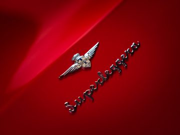 Zilverkleurig 'Touring AERO 3'-embleem en een gevleugeld logo op een levendig rood autooppervlak.