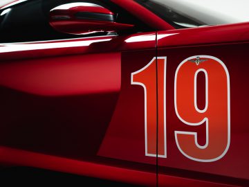 Close-up van de deur van een rode Touring AERO 3-sportwagen met het nummer '19' in het wit, met een klein logo boven het nummer.