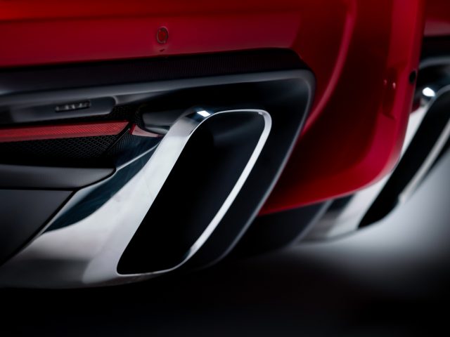 Close-up van de dubbele uitlaatpijpen van een rode Touring AERO 3-sportwagen, met de nadruk op het strakke ontwerp en de reflecterende metalen oppervlakken tegen een donkere achtergrond.