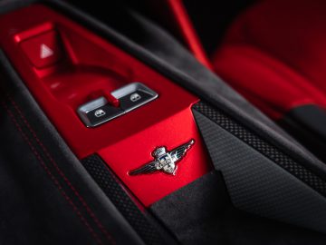 Close-up van een rood deurpaneel in een luxe auto met chromen schakelaars en een metalen Touring AERO 3-embleem.