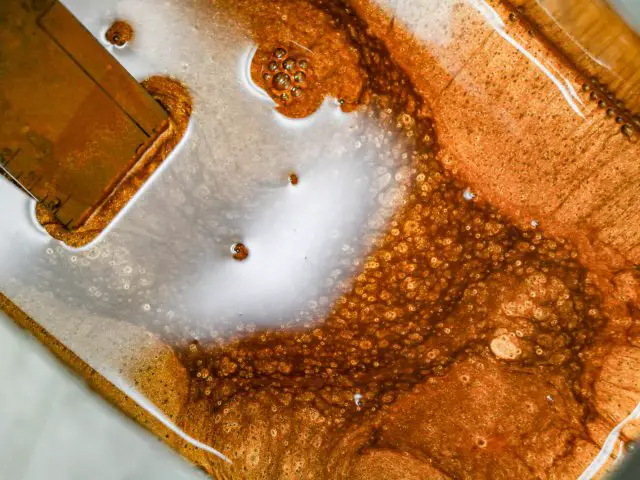 Close-up van borrelende bruine vloeistof en schuim in een vat tijdens een chemisch of kookproces tijdens een tour door AERO 3.