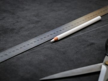 Een potlood, een liniaal en een schaar liggend op een donker gestructureerd oppervlak, horizontaal gerangschikt in een Aero 3-formatie.