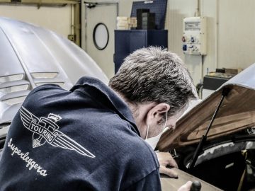 Een monteur in een werkplaats concentreert zich op het repareren van een automotor en draagt een uniform met het "Touring AERO 3"-logo.
