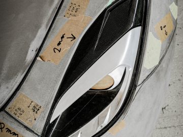 Close-up van de koplamp van een auto, gedeeltelijk bedekt met stukjes plakband, elk met handgeschreven aantekeningen, tijdens de ontwerp- of testfase van de Touring AERO 3.