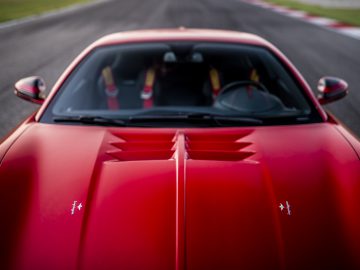 Rode Touring AERO 3 sportwagen die te hard rijdt op een racecircuit, zicht gericht op de motorkap met wazige baan en stoepranden op de achtergrond.