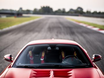 De foto toont het uitzicht over een glimmend rode Touring AERO 3-sportwagen op een racecircuit, waarbij de nadruk ligt op de motorkap en het wazige circuit verderop.