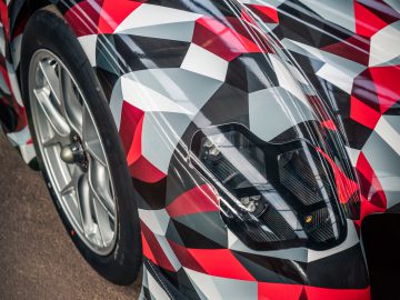 Toyota GR Super Sport met een rode, witte en zwarte camouflagefolie, buiten geparkeerd, met een close-up van de koplamp en het voorwiel.