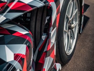Close-up van een moderne Toyota GR Super Sport-auto met een geometrisch rood, zwart en wit camopatroon, met de nadruk op het achterwiel en de spoiler.