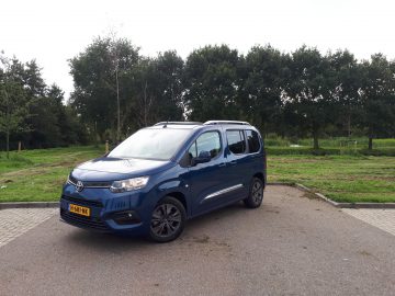 Een Toyota ProAce City Verso geparkeerd op een betonnen terrein naast een grasveld onder een bewolkte hemel.