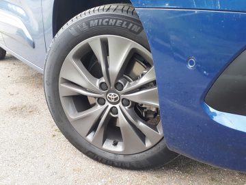 Close-up van een lichtmetalen velg van een Toyota ProAce City Verso met een Michelin-band, geparkeerd op een grindoppervlak.