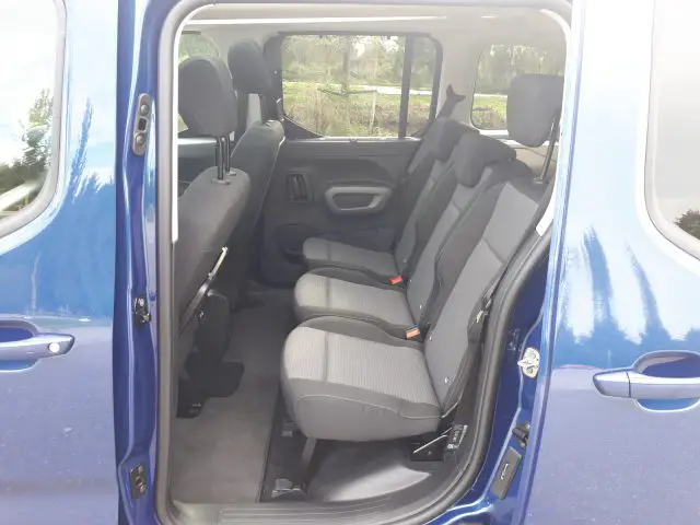Binnenaanzicht van een Toyota ProAce City Verso met open schuifdeur en drie rijen grijze stoffen stoelen.