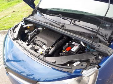 Open motorkap van een blauwe Toyota ProAce City Verso, met een gedetailleerd zicht op de motorruimte met zichtbare componenten en batterij.