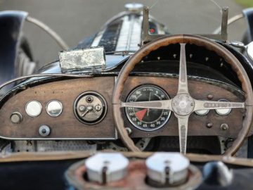 Close-up van het stuur en het dashboard van een vintage Bugatti-raceauto, met versleten houten en metalen details.