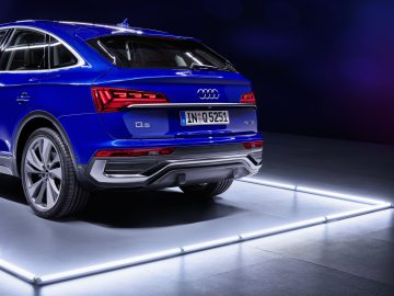 Achteraanzicht van een blauwe Audi Q5 Sportback SUV, geaccentueerd door zachte verlichting, waarbij het modelbadge en de kentekenplaat duidelijk zichtbaar zijn.
