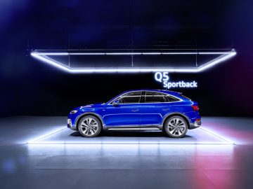 Een blauwe Audi Q5 Sportback tentoongesteld onder helderwitte lijnverlichting in een donkere showroomomgeving.