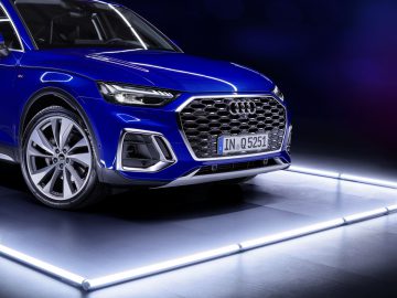 Een blauwe Audi Q5 Sportback met opvallende LED-verlichting onderstreept de auto en laat de moderne zeshoekige grille en strakke koplampen goed tot hun recht komen in een donkere omgeving.