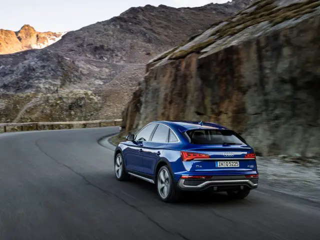 Een blauwe Audi Q5 Sportback SUV rijdt tijdens het gouden uur over een bochtige bergweg.