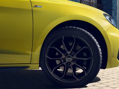 Close-up van het voorwiel van een gele Audi-auto en gedeeltelijk zicht op de carrosserie, waarbij de band en het stijlvolle velgontwerp goed zichtbaar zijn, wat de Audi-garantie benadrukt.