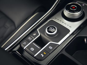 Close-up van de middenconsole van een Kia Sorento Hybrid met versnellingspook, rijmodusknop en verschillende bedieningsknoppen.