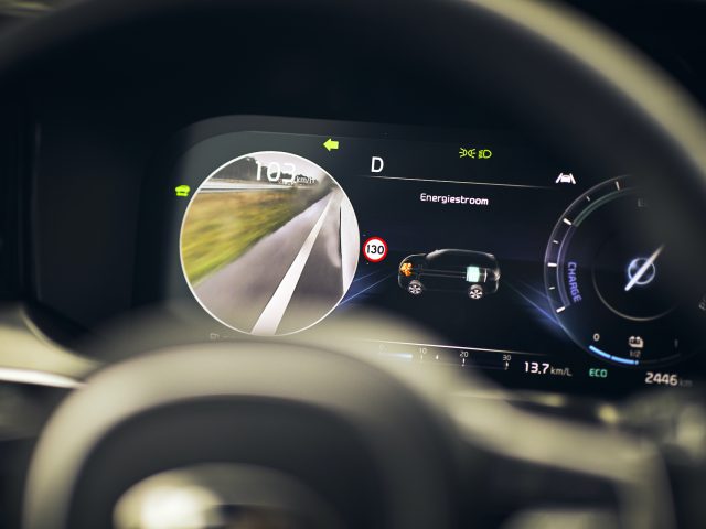 Close-up van het digitale dashboard van een Kia Sorento Hybrid met snelheid, batterijniveau en camerabeelden in de achteruitkijkspiegel.