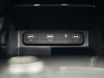 Close-up van het interieur van een Kia Sorento Hybrid met twee USB-poorten en een symbool voor een draadloos oplaadpad op een dashboard.