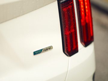 Close-up van de achterkant van een witte Kia Sorento Hybrid met een 'eco hybride'-badge naast verticale rode achterlichten, op een regenachtige dag.