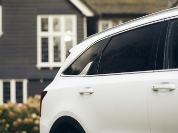 Witte Kia Sorento Hybrid geparkeerd voor een huis met donkere gevelbeplating, met de nadruk op de achterkant van het voertuig.