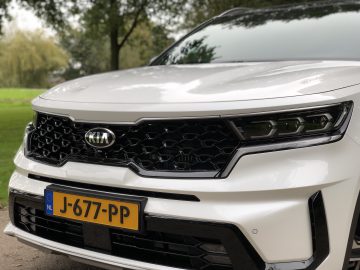 Close-up van de grille en koplampen van een witte Kia Sorento Hybrid, met een opvallend zeshoekig patroon en een zichtbare Europese kentekenplaat.