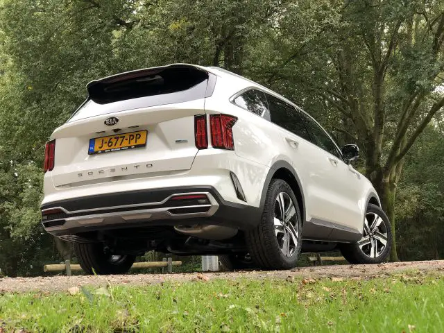 Witte Kia Sorento hybride SUV geparkeerd op een pad met weelderige groene bomen op de achtergrond.