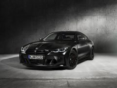 Een zwarte BMW M4 Competition x KITH sportcoupé geparkeerd in een betonnen garage, met een agressieve styling en een strak design.