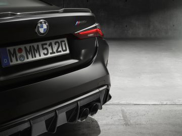 Achteraanzicht van een zwarte BMW M4 Competition x KITH met opvallende achterlichten en viervoudige uitlaatpijpen, geparkeerd in een slecht verlichte garage.