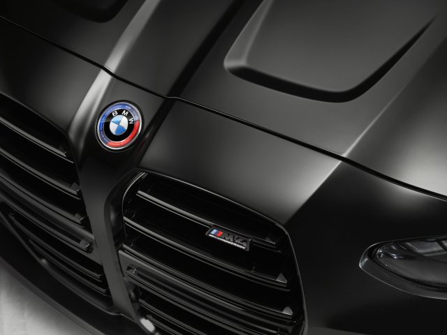 Close-up van een zwarte BMW M4 Competition x KITH-autokap met het BMW-logo en het M4-embleem zichtbaar, wat het strakke ontwerp en de details van de auto laat zien.