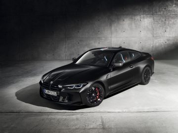 Een zwarte BMW M4 Competition x KITH geparkeerd in een betonnen garage, met strakke carrosserielijnen en opvallende koplampen, die een sportief en agressief ontwerp laten zien.